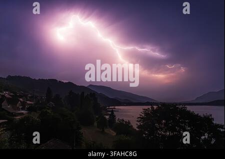 Massenblitz eines Gewitters am Himmel, der ein kleines Dorf an einem See in der Nacht im Südosten Frankreichs beleuchtet Stockfoto