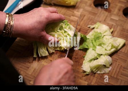 Kopfsalat mit Messer auf Holzschneidebrett schneiden. Frau schneidet frischen Salat. Stockfoto