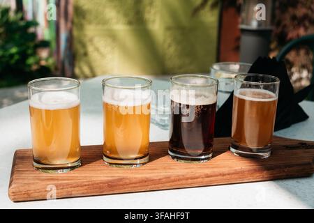 Verschiedene Craft-Bier-Proben, serviert in klaren Gläsern auf einem Holzteller. Frische Brauerei-Proben schaffen ein modernes Bar- und Verkostungskonzept. Stockfoto