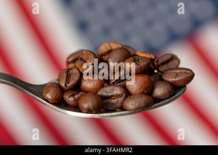 Kaffeebohnen ruhen auf einem Löffel vor einem verschwommenen Hintergrund der amerikanischen Flagge. Stockfoto