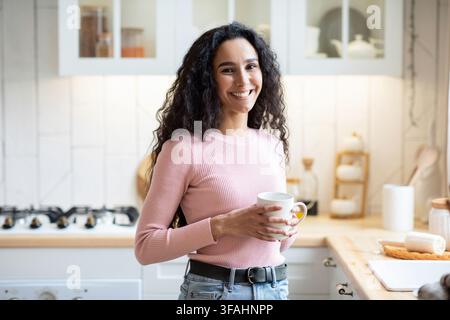 Lächelnde Brünette Frau Mit Tasse Kaffee In Den Händen Stehen In Der Küche Stockfoto