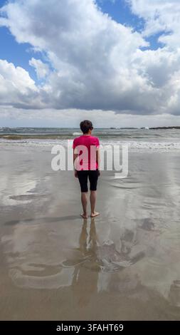 Frau steht barfuß auf nassem Sand und denkt am Meer über das Leben nach Stockfoto