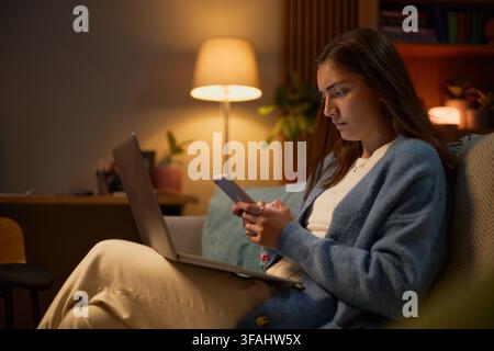 Frau nutzt Smartphone und Laptop während der Arbeit zu Hause am Abend Stockfoto
