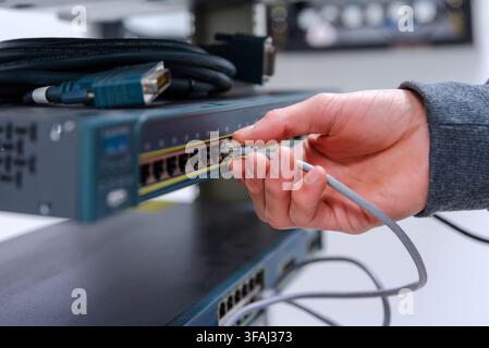 Nahaufnahme der Hand eines Technikers, der ein graues Ethernet-Netzwerkkabel in einen Router- oder Switch-Port steckt. Stockfoto