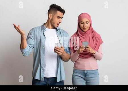 Datenschutzkonzept. Porträt eines schockierten arabischen Mannes, der das Smartphone der muslimischen Frau ansah Stockfoto