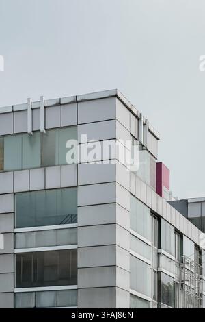 Niedrigwinklige Außenaufnahme einer modernen Bürogebäude-Ecke mit grauen Metall-Verbundwandplatten und großen Glasfassadenfenstern Stockfoto