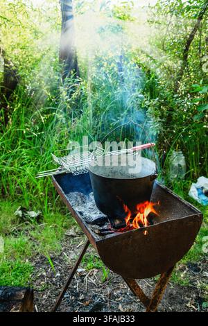 Vorbereiten von warmen Speisen in einem großen Campingtopf über einem offenen Feuer während eines Picknicks oder Wanderausflugs in der Natur Stockfoto