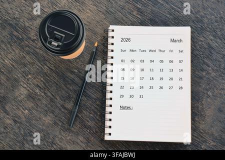 Schreibtischkalender für März 2026 mit Wegwerf-Kaffeebecher und Stift auf Holztablett. Direkt von oben. Flat Lay Stockfoto