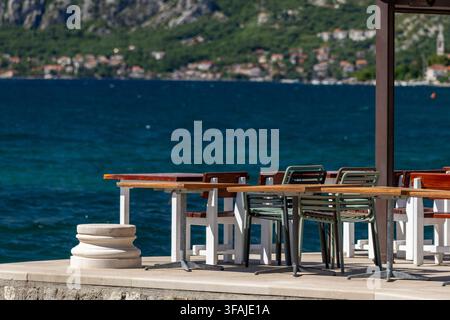Leere Tische eines Restaurants am Meer mit Blick auf die blaue Bucht Stockfoto