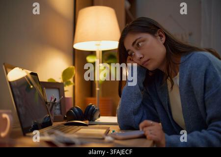 Müde Frau schaut auf Laptop-Bildschirm und arbeitet spät in der Nacht Stockfoto