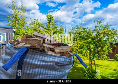 Nahaufnahme eines großen Beutels gefüllt mit geliefertem Birkenholz neben Apfelbäumen in einem sonnigen Garten. Schweden. Stockfoto