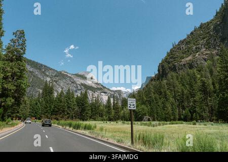 Autos fahren eine malerische Straße durch das Yosemite-Tal vorbei an einem Geschwindigkeitsbegrenzungsschild mit 25 mph, während auf beiden Seiten Granitkuppeln und Kiefernwald aufragen. Stockfoto
