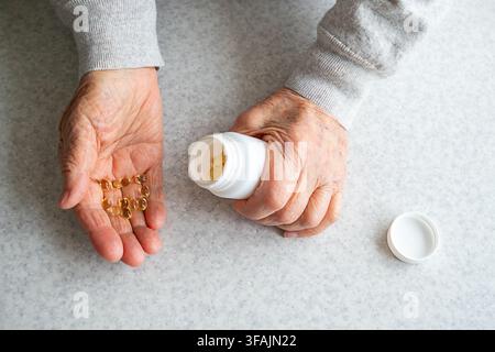 Ältere Hände schütten Vitaminkapseln aus einer Medikamentenflasche für die tägliche Gesundheits- und Pflegeroutine Stockfoto