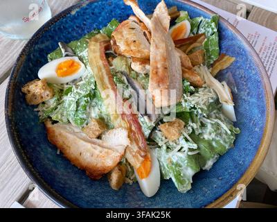 Caesar-Salat mit Hühnchen, gekochten Eiern und Croutons in einer blauen Schüssel Stockfoto