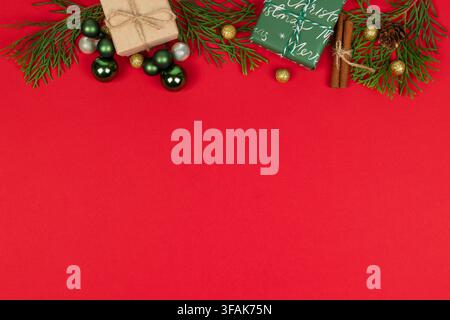 Weihnachts-Flat-Lay mit grünen Ornamenten, Tannenzweigen, verpackten Geschenken, Zimtstangen, Tannenzapfen, goldenen Akzenten und rotem Hintergrund Stockfoto