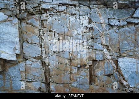 Nahaufnahme einer grauen Felsoberfläche mit vertikalen Klüften und Mineraladern. Natürliche geologische Textur mit verwittertem Stein und geschichteten Formationen. Stockfoto