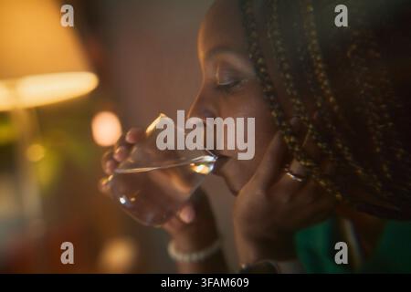 Schwarze Frau trinkt ein Glas Wasser für die Abend-Wellness-Routine Stockfoto