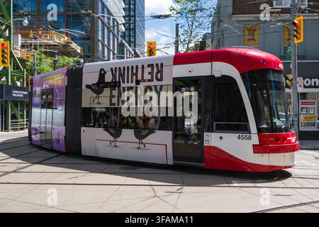 Im Herzen von Toronto, Ontario, navigiert eine moderne Straßenbahn durch die belebten Stadtstraßen. Dieses öffentliche Verkehrsmittel, geschmückt mit Grafiken Stockfoto
