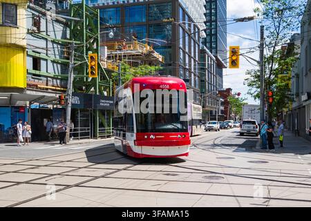 Erleben Sie die lebendige Energie der Innenstadt von Toronto, während eine Straßenbahn die belebte Kreuzung von Queen und Spadina überquert. Dieser zentrale Knotenpunkt präsentiert Stockfoto