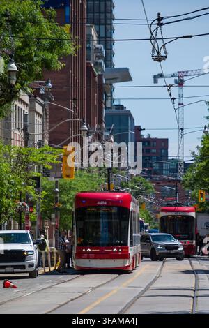 Erleben Sie die lebhafte Energie von Toronto entlang einer geschäftigen Stadtstraße. Eine moderne Straßenbahn navigiert die Fahrbahn und teilt den Raum mit Autos und pe Stockfoto