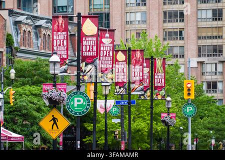 Erleben Sie die lebendige Energie von Toronto am historischen St. Lawrence Market. Diese geschäftige Straßenlandschaft zeigt die ikonischen Flaggen des Marktes, die signalisieren Stockfoto