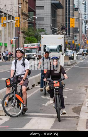 Erleben Sie die lebendige Energie von Toronto, während Radfahrer eine belebte Innenstadtstraße befahren. Hoch aufragende Gebäude bilden eine dramatische Kulisse für dieses Alltags Stockfoto