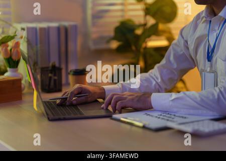 Abgeschnittene Hände eines Geschäftsmannes, der spät im Büro am Schreibtisch auf einem Laptop tippt Stockfoto