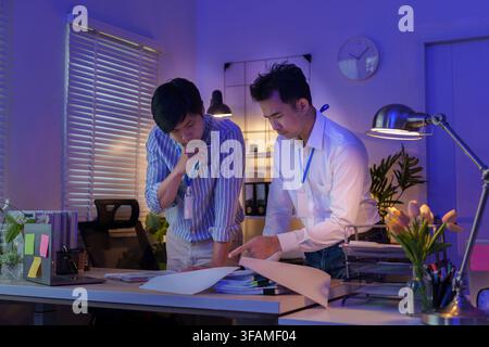Zwei asiatische Geschäftsleute arbeiten gemeinsam an Finanzberichten, während sie spät im Büro arbeiten Stockfoto