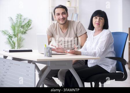 Junger männlicher Angestellter erklärt einer alten weiblichen Kollegin, wie man Computer benutzt Stockfoto