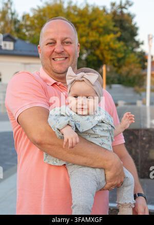 Ein Mann hält ein Baby in einer Außenumgebung und schafft eine warme und familiäre Atmosphäre. Das Nahaufnahme-Porträt fängt den zarten Moment zwischen Stockfoto