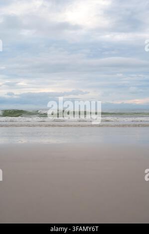 Niedrigwinklige Ansicht von Meereswellen, die unter einem bewölkten Himmel an einem Sandstrand brechen. Stockfoto