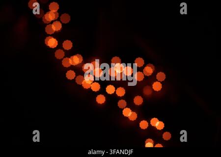Abstrakter Hintergrund mit leuchtenden orangefarbenen Bokeh-Lichtpunkten, die in einer gewundenen Form auf einem dunklen schwarzen Hintergrund angeordnet sind. Stockfoto