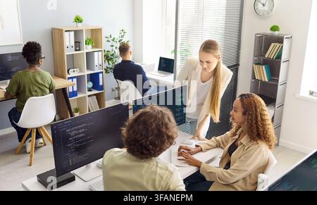 Team von Programmierern diskutiert Softwareprojekt an Schreibtischen in hellem Tech-Büro Stockfoto
