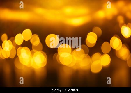 Warme goldene unscharfe Bokeh-Lichter mit leuchtenden Reflexionen und dunklem bernsteinfarbenem Hintergrund für festliche Überlagerung und Design Stockfoto