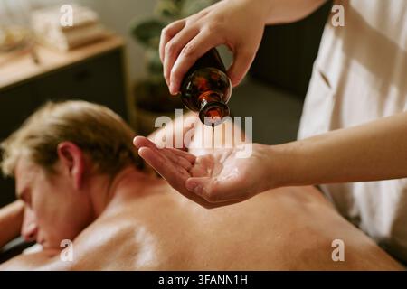 Masseur gießt ätherisches Öl für einen Mann, der eine Rückenmassage erhält Stockfoto