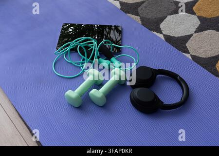 Heimtrainingsgerät mit Hanteln, Springseil, Kopfhörern und Tablet, arrangiert auf einer Trainingsmatte. Konzept des Online-Fitnesstrainings, aktiver Lebensstil Stockfoto