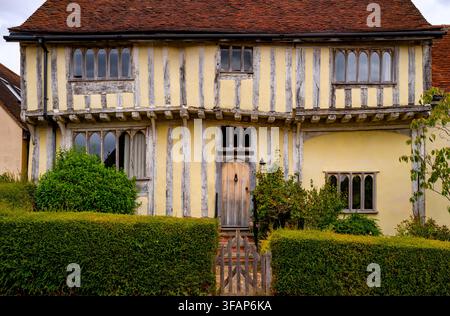 Mittelalterliches Fachwerkhaus mit gelben kalkweißen Wänden, freiliegenden Eichenbalken, gewölbten gotischen Fenstern und einer Holztür hinter einem geschnittenen Heck in Lavenh Stockfoto