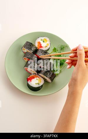 Frauenhand, die mit Stäbchen eine Sushirolle aufnimmt Stockfoto