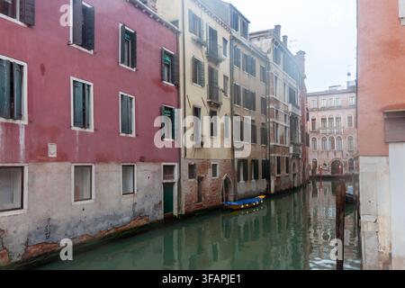 Schmaler venezianischer Kanal, gesäumt von farbenfrohen historischen Wohnhäusern und einem kleinen Boot an einem bewölkten Tag, Italien Stockfoto