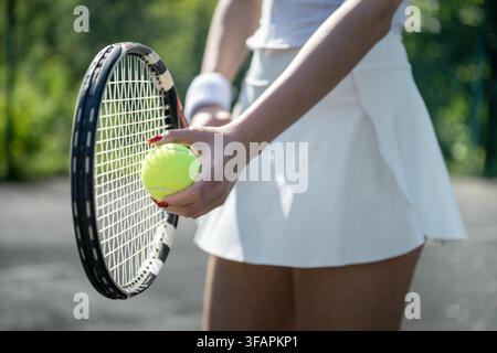 Nahaufnahme einer Tennisspielerin, die einen gelben Ball gegen die Schlägersaite hält, während sie sich auf den Aufschlag auf einem Außenplatz vorbereitet. Stockfoto