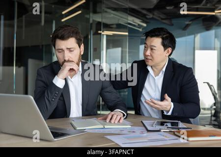 Asiatischer Geschäftsmann tröstet traurigen männlichen Kollegen, der Stress und Probleme bei der Arbeit erlebt, zeigt Empathie und bietet emotionale Unterstützung einem gestressten Mitarbeiter in der Büroumgebung Stockfoto