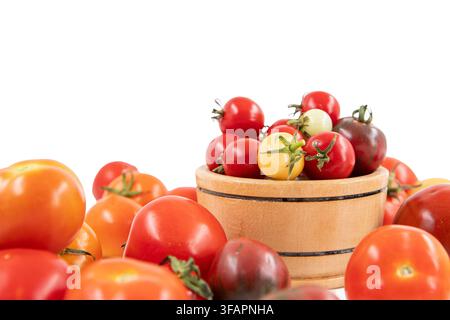 Verschiedene farbenfrohe Tomaten, arrangiert in einem Weidenkorb und einer kleinen Holzschale Stockfoto