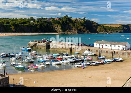 Tenby Harbour Pier und festgemachte Boote bei Ebbe in Pembrokeshire, Wales, mit steinernem Kai, sandigem Meeresboden, North Beach und bewaldeter Landzunge dahinter Stockfoto