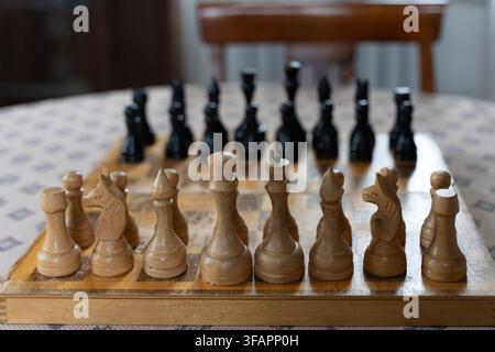 Vintage-Schachfiguren aus Holz, die auf einem abgenutzten Schachbrett im Innenraum angeordnet sind, fotografiert mit selektiver Schärfentiefe. Stockfoto