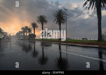 Nasse Küstenstraße und Palmen bei Sonnenuntergang in Kapstadt Stockfoto