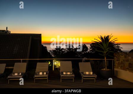 Sonnenliegen auf der Terrasse mit Sonnenuntergang über dem Ozean in Kapstadt Stockfoto