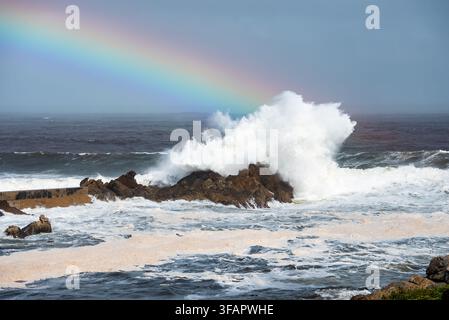 Ozeanwellen schlagen gegen die felsige Küste unter einem Regenbogen in Kapstadt Stockfoto