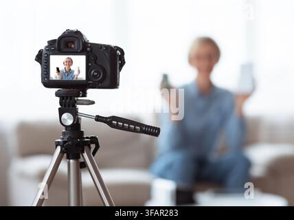 Junge kaukasische Frau, die Videoinhalte für ihren Tech-Blog zu Hause aufzeichnet, selektiver Fokus auf Kamera mit Vorschaubildschirm Stockfoto