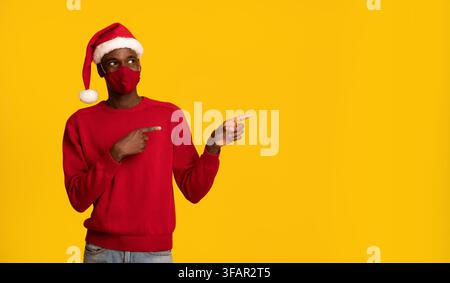 Schwarzer Mann In Schutzmaske Und Weihnachtsmütze Zeigt Auf Speicherplatz Kopieren Stockfoto