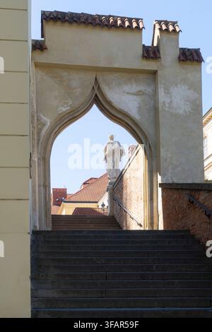 Brno, Tschechische Republik. 12. August 2026. Eine steinerne Treppe führt zu einem gewölbten Tor. Durch das Gewölbe steht eine Statue einer Gestalt in Gewändern auf einem r Stockfoto
